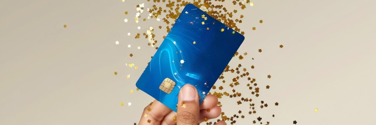 A hand holding up a generic blue credit card with gold glitter falling around it.