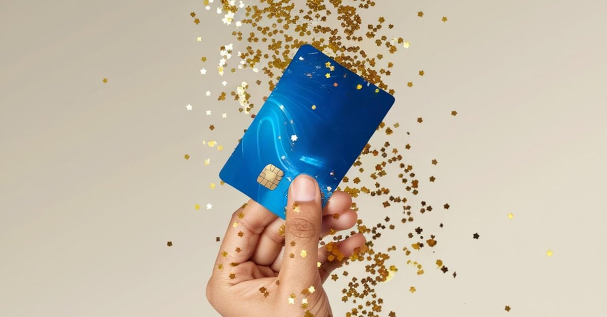 A hand holding up a generic blue credit card with gold glitter falling around it.