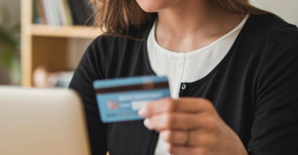 Woman holds credit cards in front of her while she uses laptop.