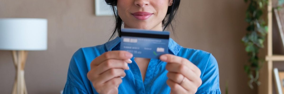 Woman in blue holding up a credit card with two hands.
