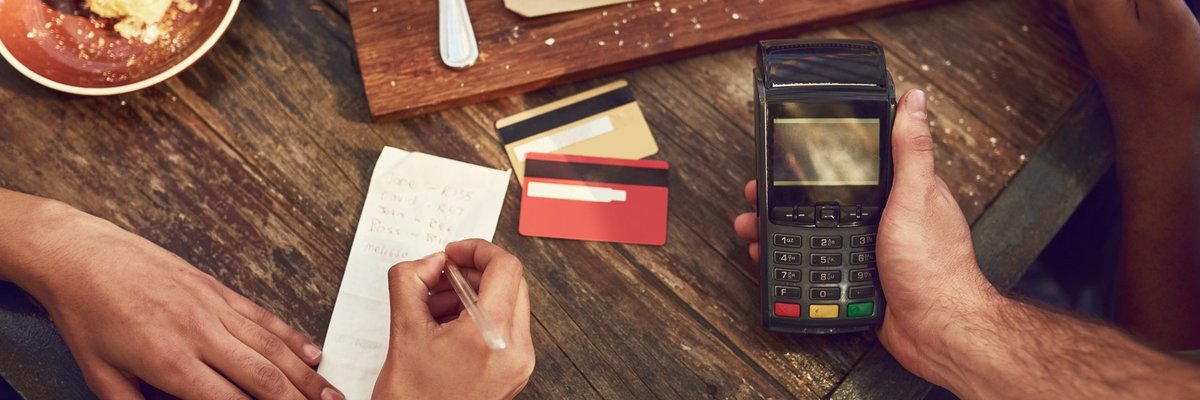 A woman signing the receipt for her credit card payment while the waiter holds the card reader after finishing lunch at a restaurant.