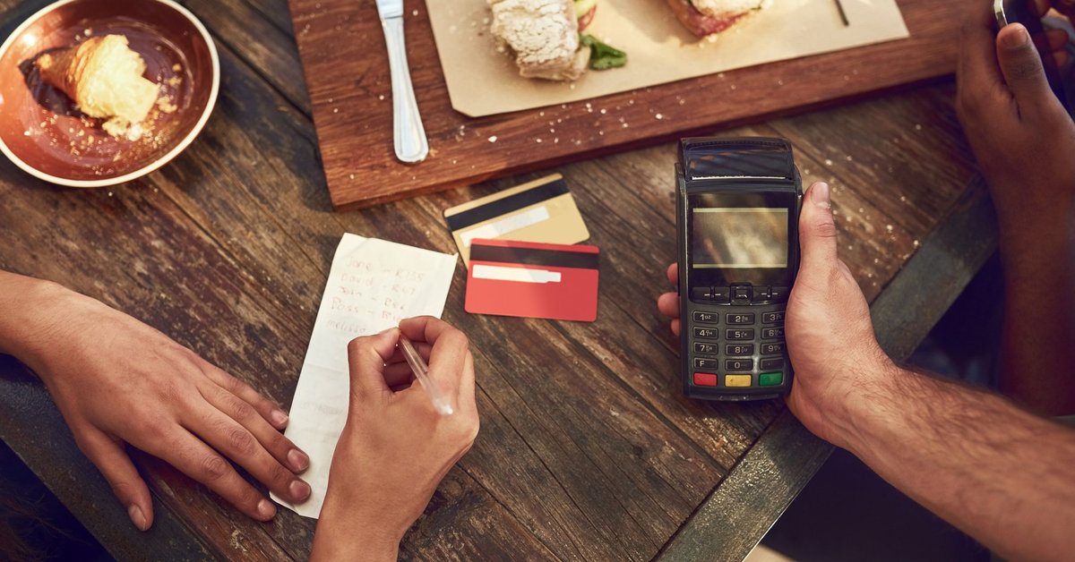 A woman signing the receipt for her credit card payment while the waiter holds the card reader after finishing lunch at a restaurant.