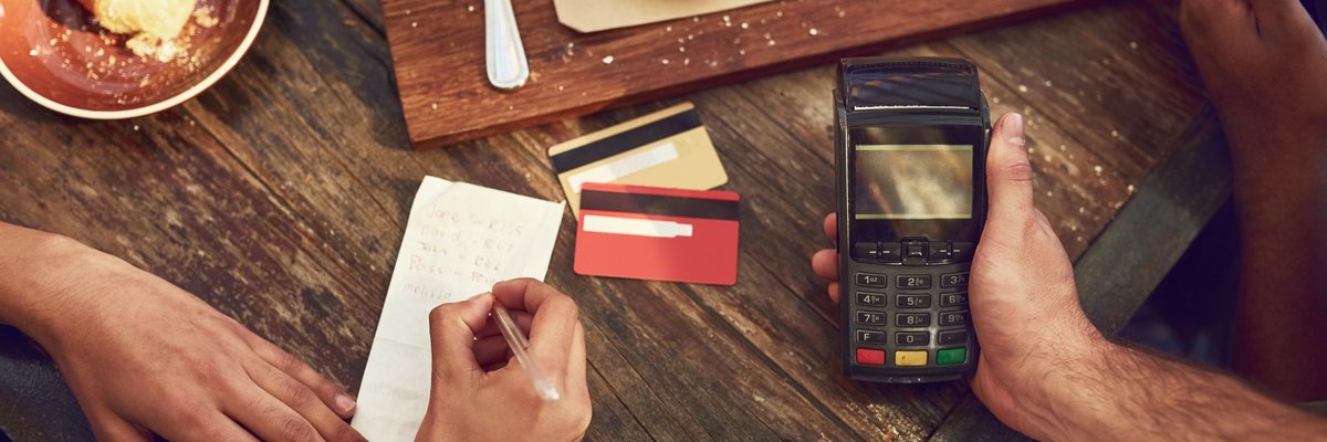 A woman signing the receipt for her credit card payment while the waiter holds the card reader after finishing lunch at a restaurant.
