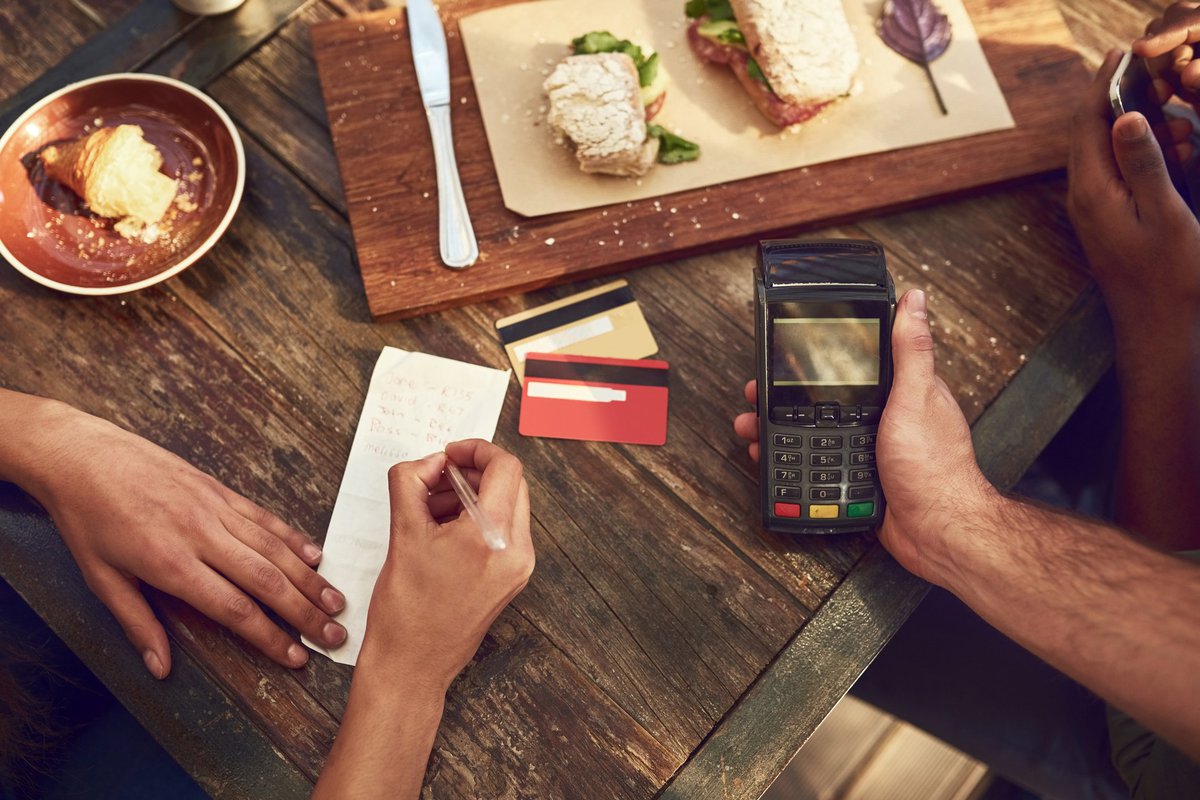 A woman signing the receipt for her credit card payment while the waiter holds the card reader after finishing lunch at a restaurant.