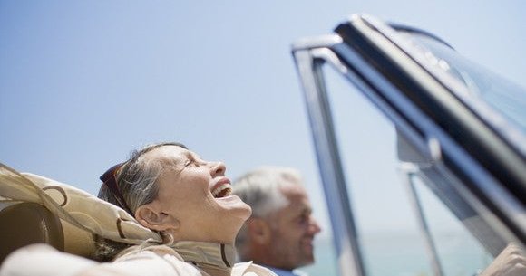 older couple smiling as they drive in a convertible