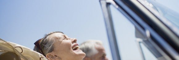older couple smiling as they drive in a convertible