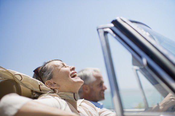 older couple smiling as they drive in a convertible