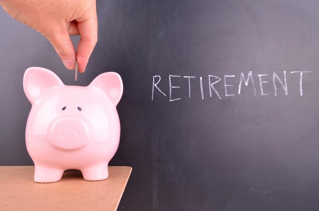 A hand putting coins into a piggy bank with the word Retirement behind it on a chalk board.