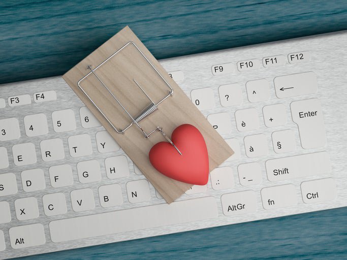 A mouse trap baited with a plastic heart sits on top of a keyboard.
