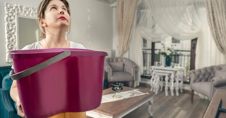 A woman holds a bucket to catch water from a roof leak.