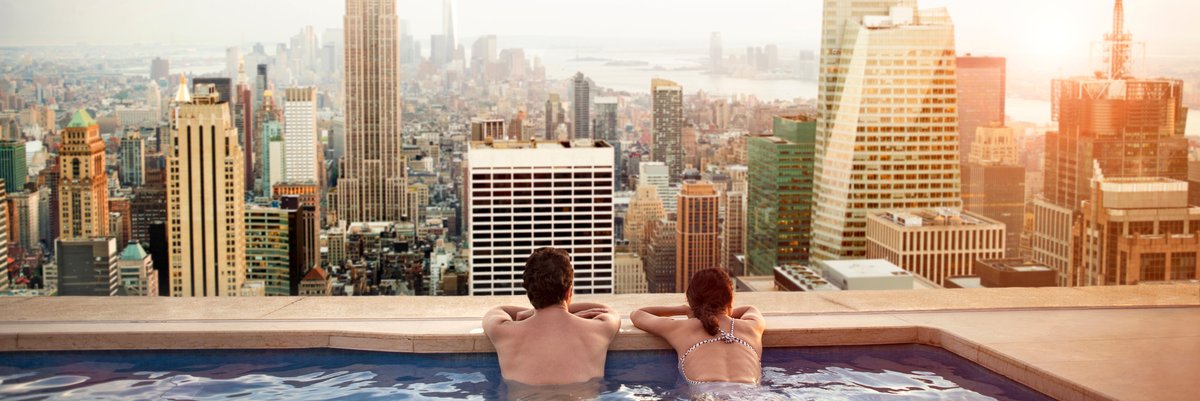 Couple enjoys city skyline view from rooftop pool.