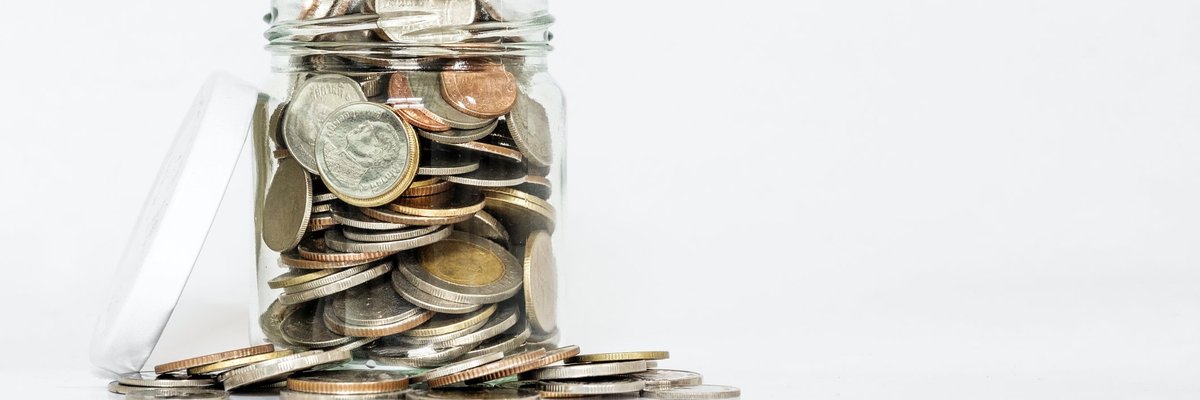 A glass jar with its lid open is overflowing with coins.