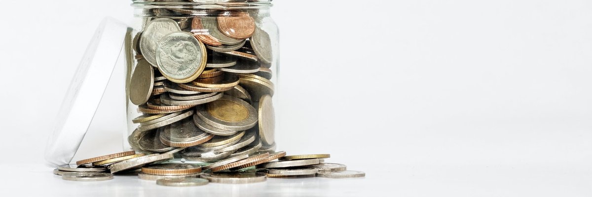 A glass jar with its lid open is overflowing with coins.