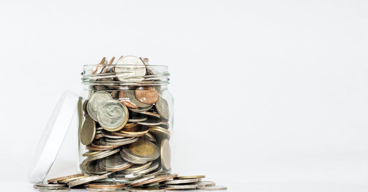 A glass jar with its lid open is overflowing with coins.