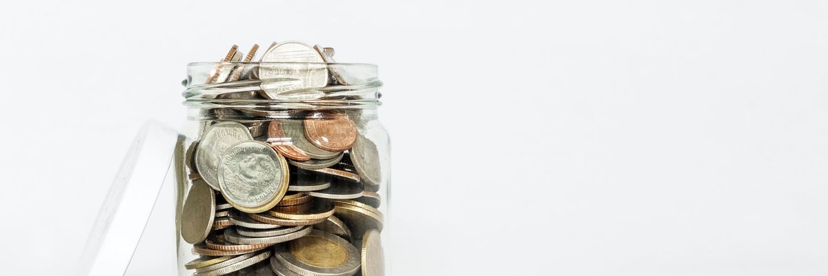 A glass jar with its lid open is overflowing with coins.