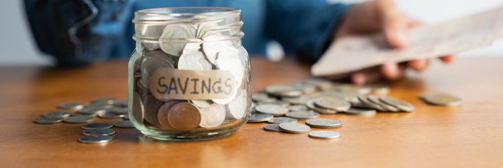 A woman puts a coin into a jar labelled "savings."
