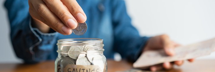 A woman puts a coin into a jar labelled "savings."