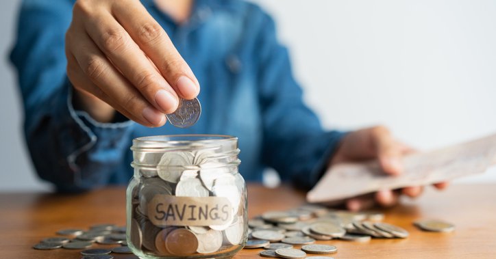 A woman puts a coin into a jar labelled "savings."