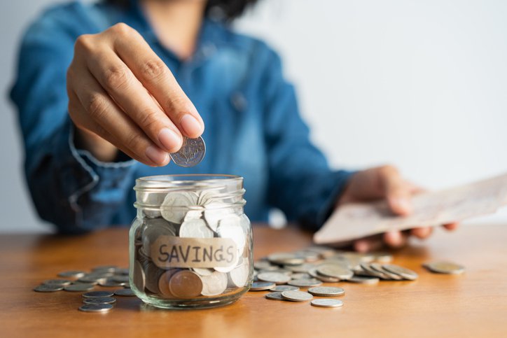 A woman puts a coin into a jar labelled "savings."