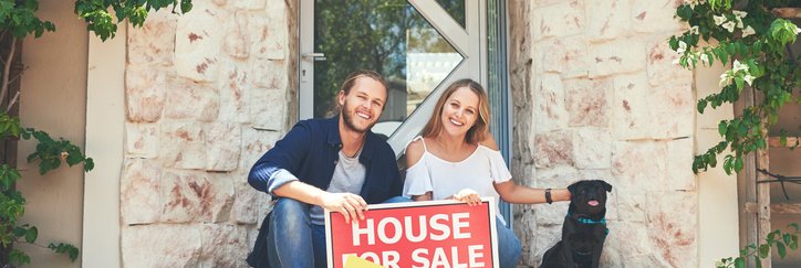 A couple on a porch, holding a "sold" sign.