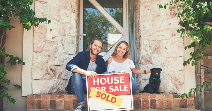 A couple on a porch, holding a "sold" sign.