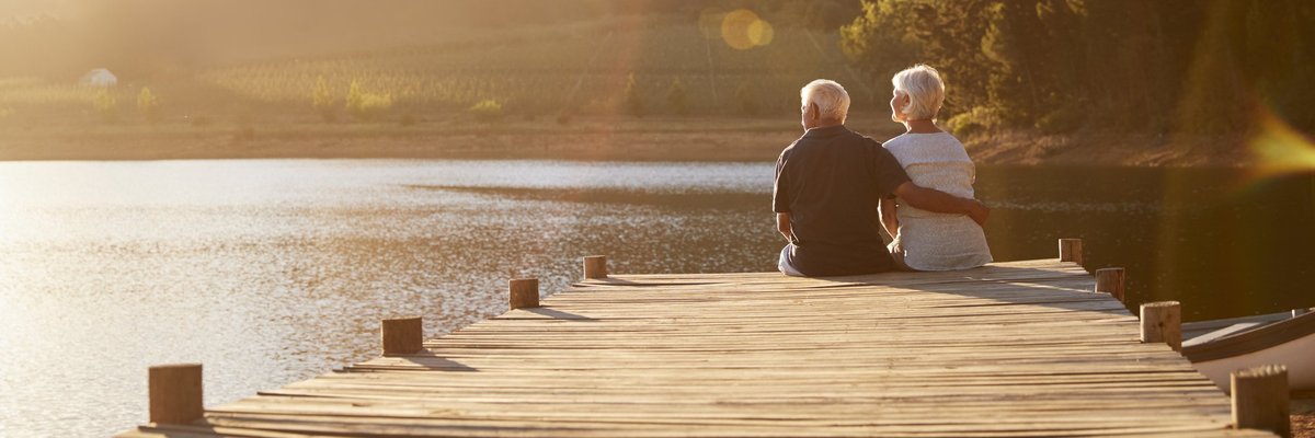 A senior man and woman sitting at the end of a dock on a lake.