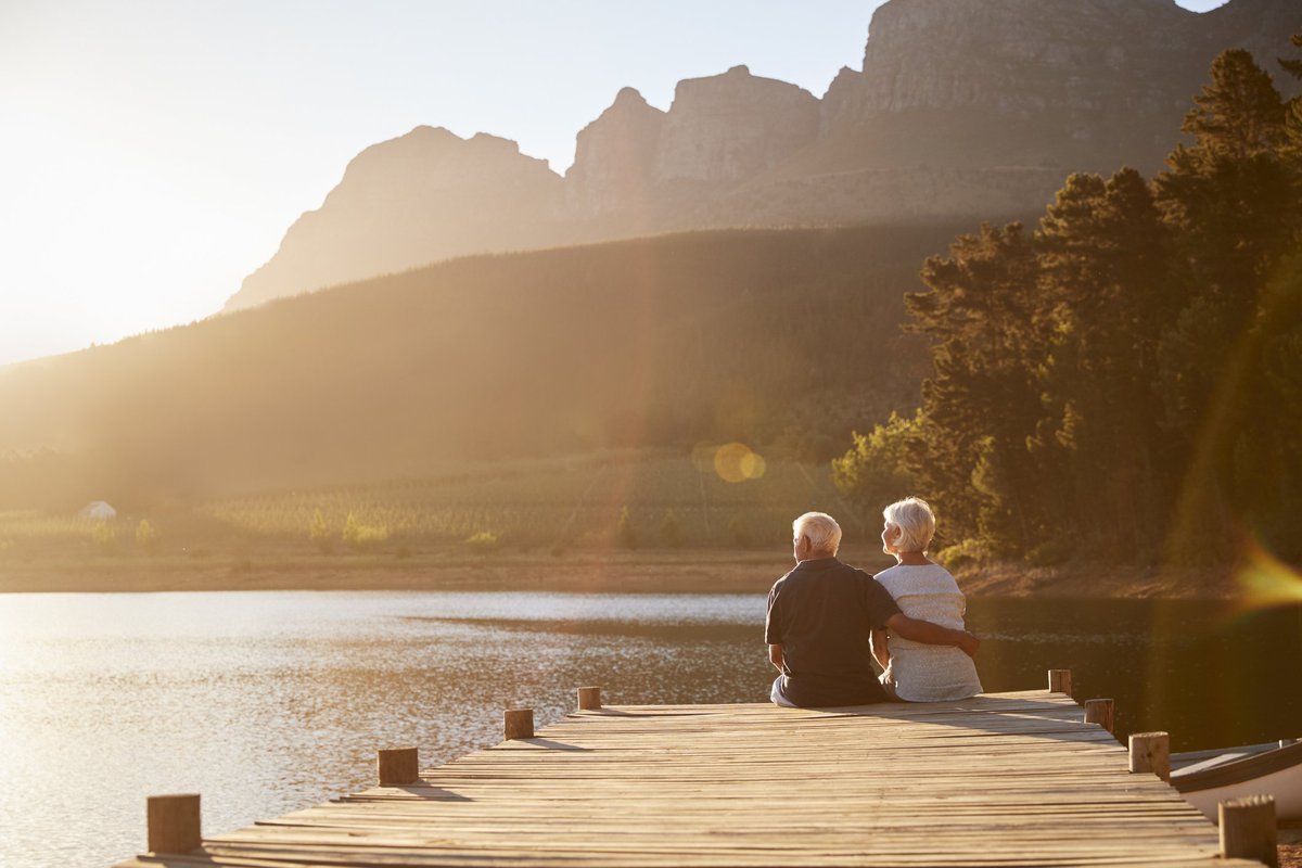 senior man and woman sitting at the end of a dock on a lake_retirement relaxing vacation