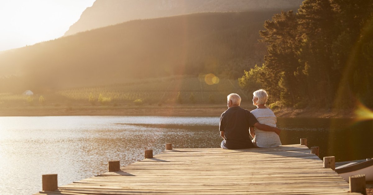 A senior man and woman sitting at the end of a dock on a lake.