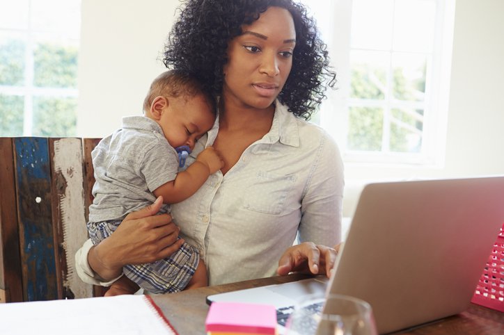 A mother holds an infant while she works on her computer.