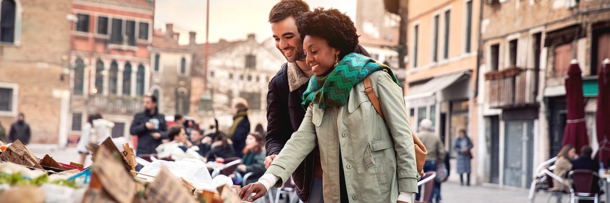A smiling couple on vacation shopping at an outdoor craft market.