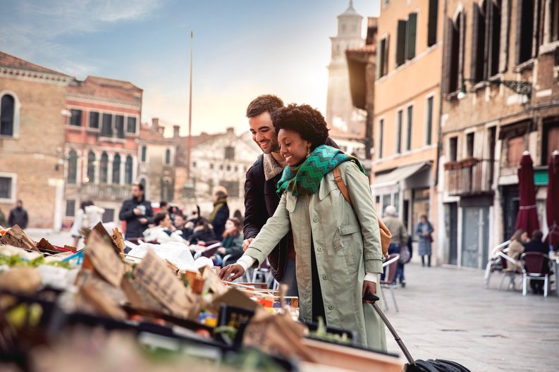 A smiling couple on vacation shopping at an outdoor craft market.