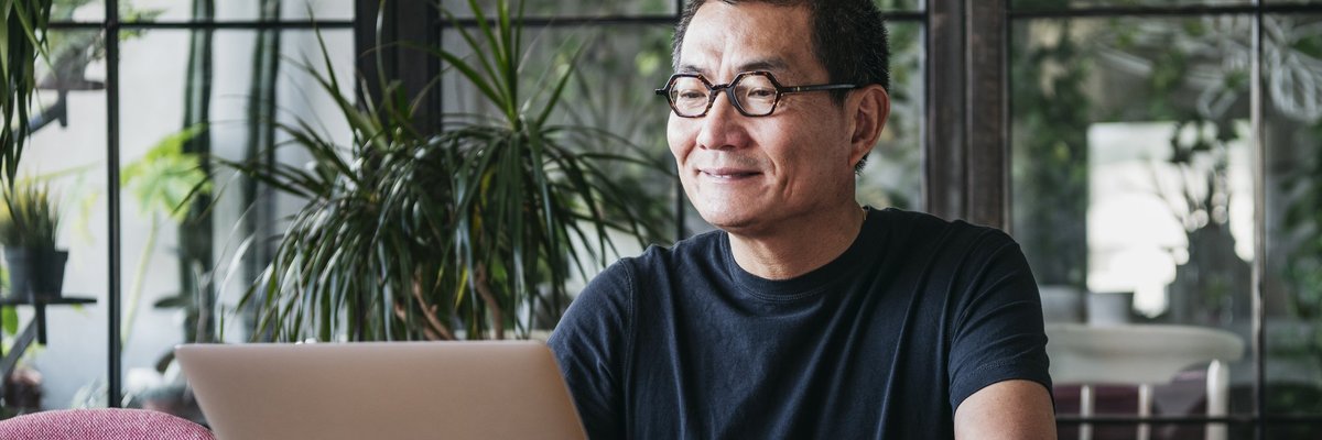A smiling man working on a laptop in a room full of plants.