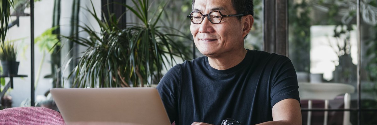 A smiling man working on a laptop in a room full of plants.