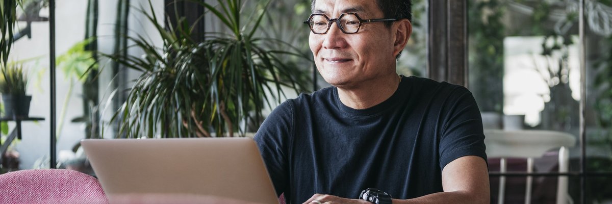 A smiling man working on a laptop in a room full of plants.