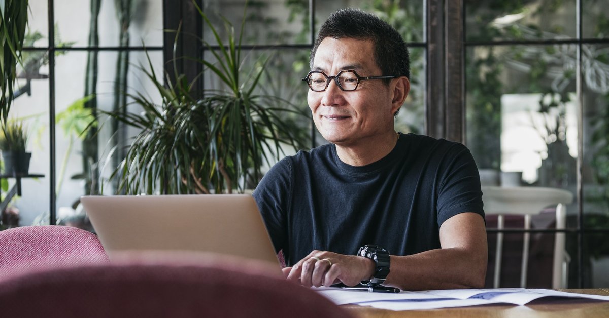 A smiling man working on a laptop in a room full of plants.
