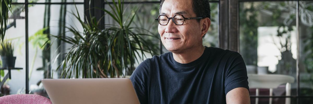 A smiling man working on a laptop in a room full of plants.