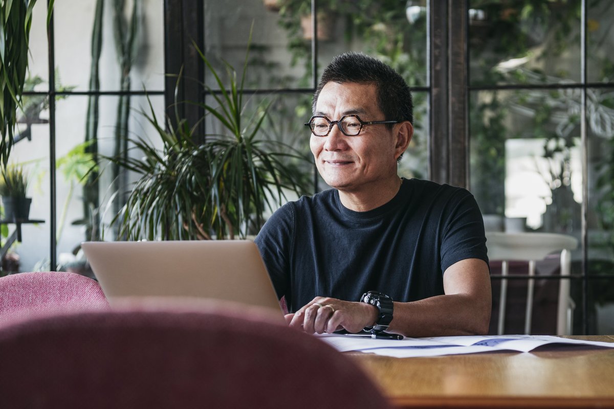 A smiling man working on a laptop in a room full of plants.