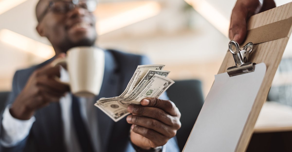 smiling young man holding a coffee mug and handing cash to a waiter