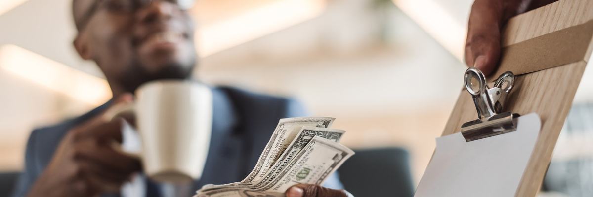 smiling young man holding a coffee mug and handing cash to a waiter