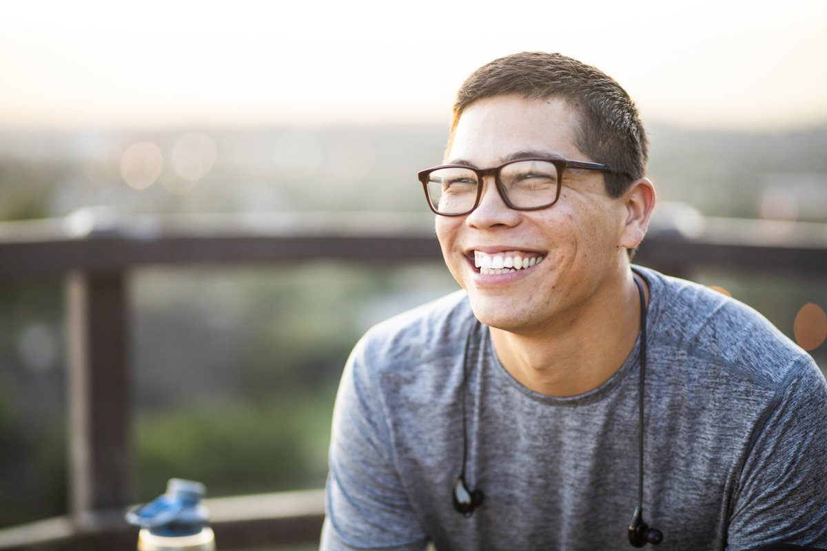 A smiling young man sitting at an outdoor patio.