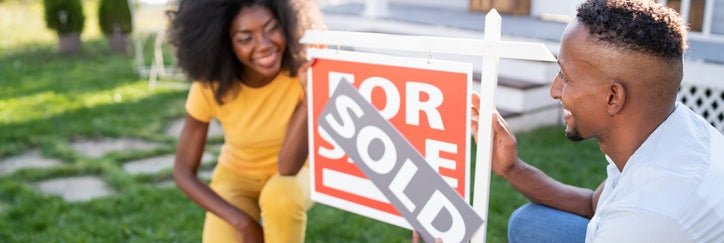 A couple putting "sold" onto a house for sale sign.
