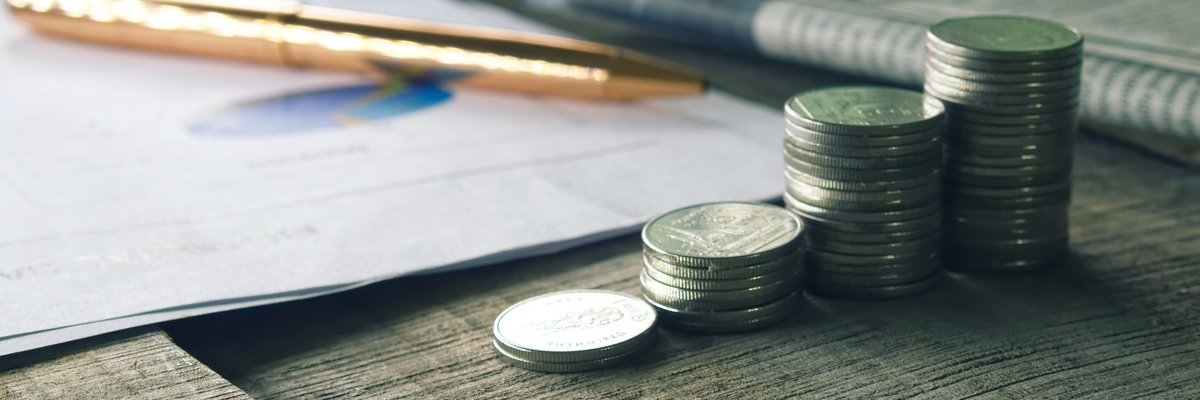 Stack of coins and gold pen next to newspaper