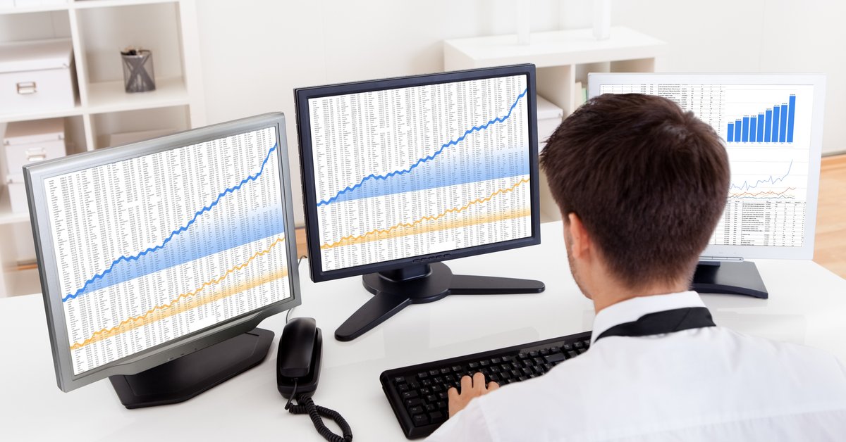 A man using a computer with three different monitors full of charts and graphs.