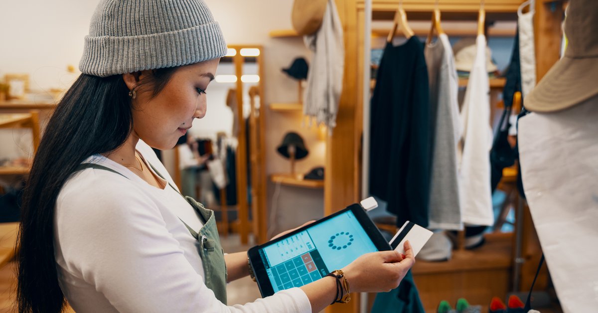 A female clerk at a clothing store swiping a credit card on a payment tablet.