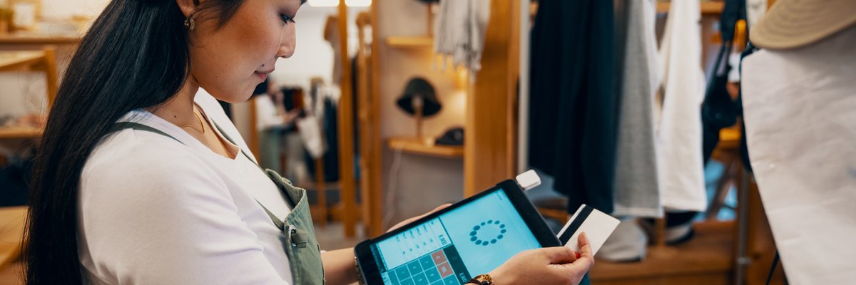 A female clerk at a clothing store swiping a credit card on a payment tablet.