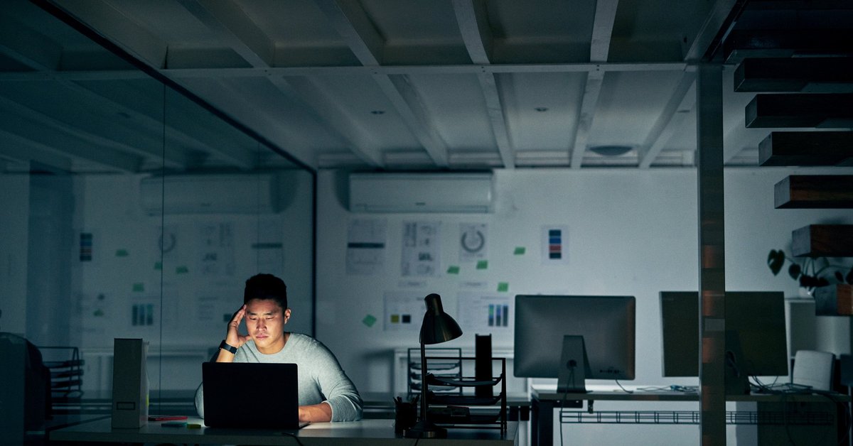 A stressed young man sitting in front of a laptop in a dark office.