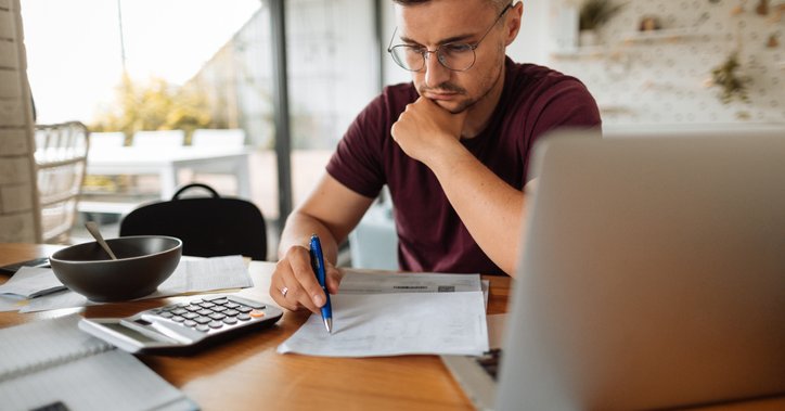A man looking stressed while going through his bills next to his open laptop.