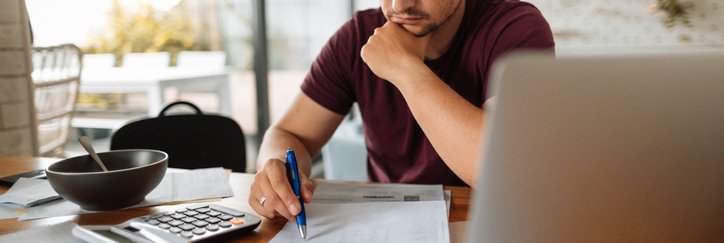 A man looking stressed while going through his bills next to his open laptop.