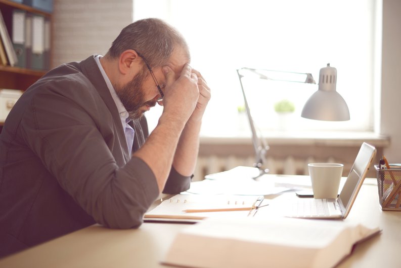 A stressed man working at a desk with his head in his hands.