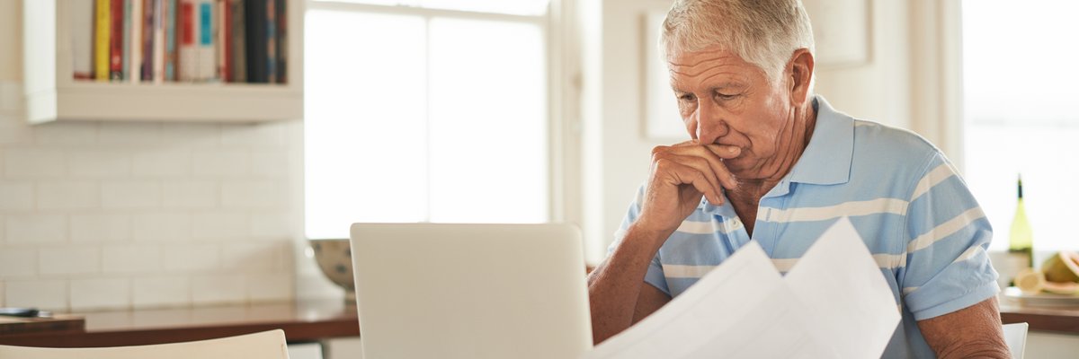 A stressed person looking through papers and sitting in front of a laptop at a kitchen counter.